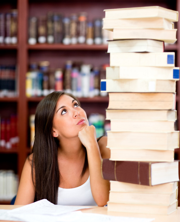 Busy female student with a pile of books at the library